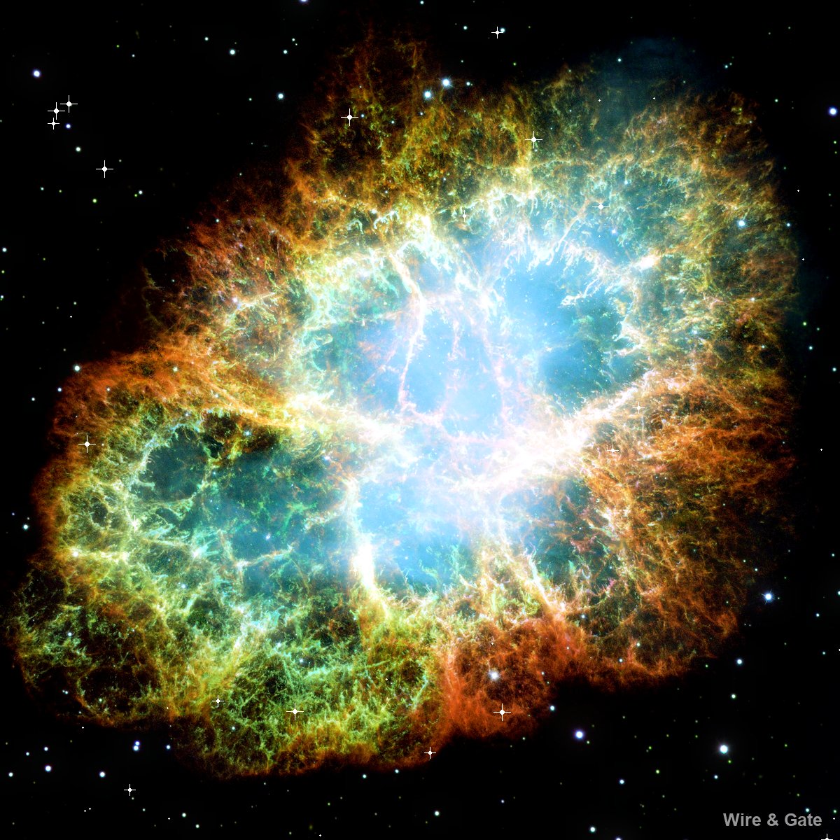 A cloud of orange, yellow and green filaments around a pale blue core, against a starry black sky
